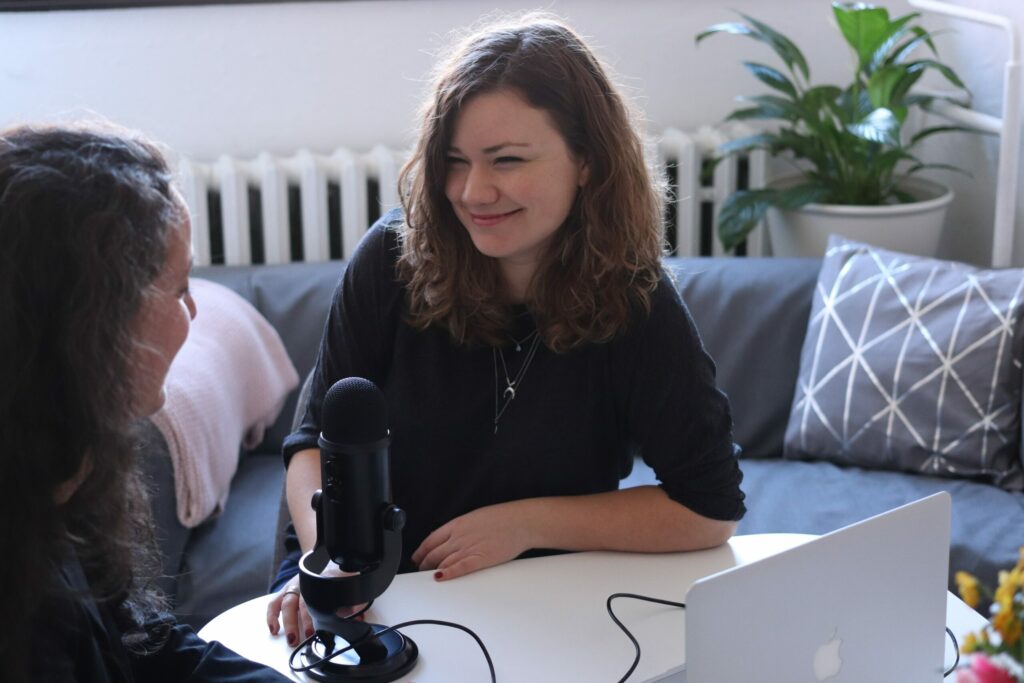 Two women recording podcast at laptop
